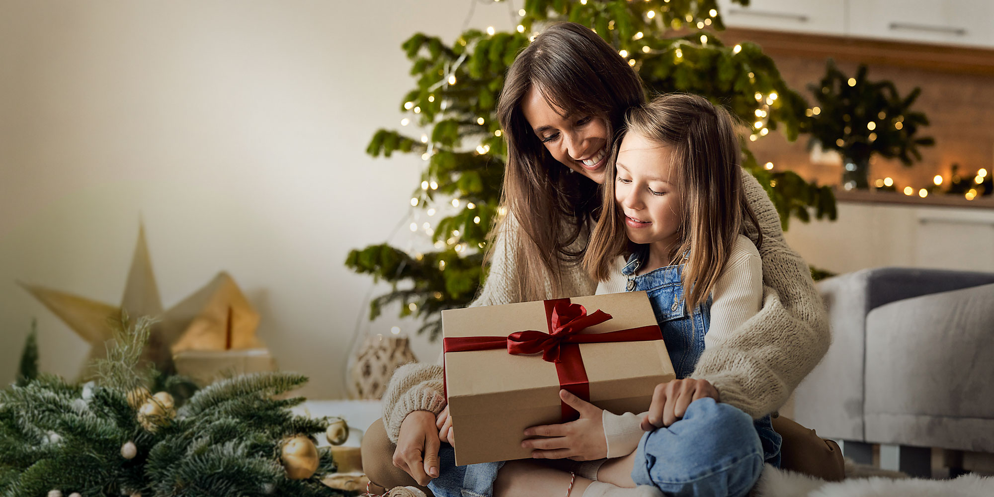 Eine Mutter packt mit ihrer Tochter Geschenke vor dem Weihnachtsbaum aus.