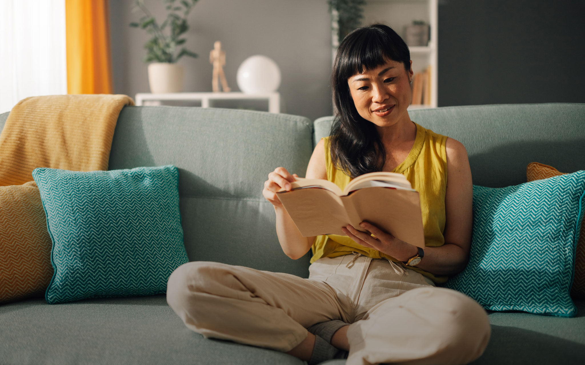 Frau, die bequem auf einem Sofa mit bunten Kissen liest.