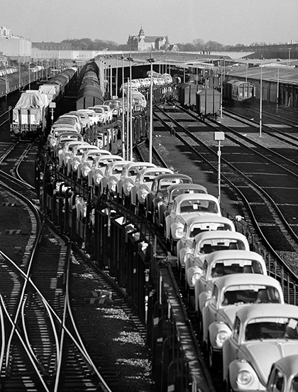 Schwarz-Weiss-Aufnahme von Heinrich Heidersberger eines Gueterzuges, beladen mit VW-Kaefern und dem Schloss Wolfsburg im Hintergrund