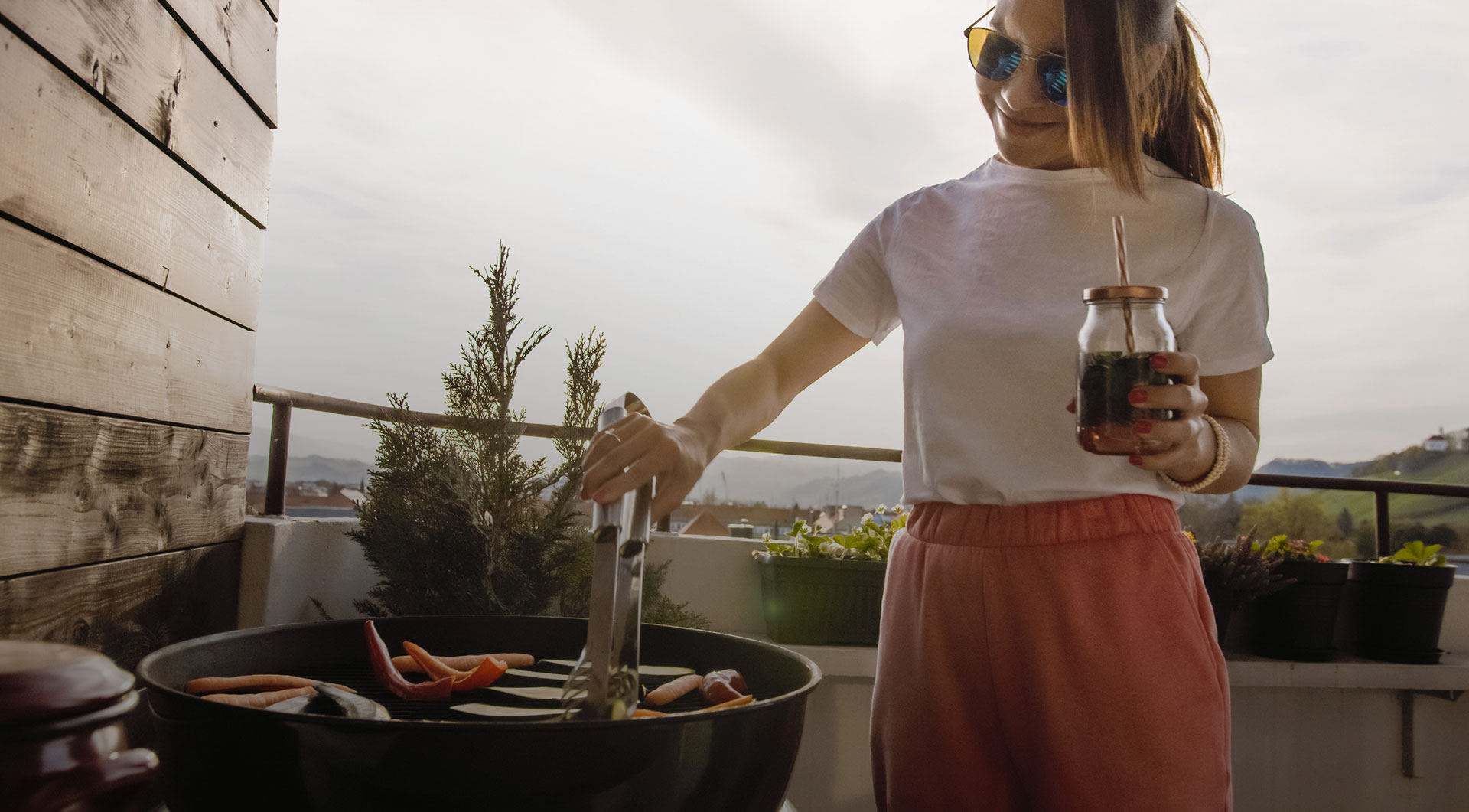 Eine fröhliche Frau steht auf einem Balkon und grillt