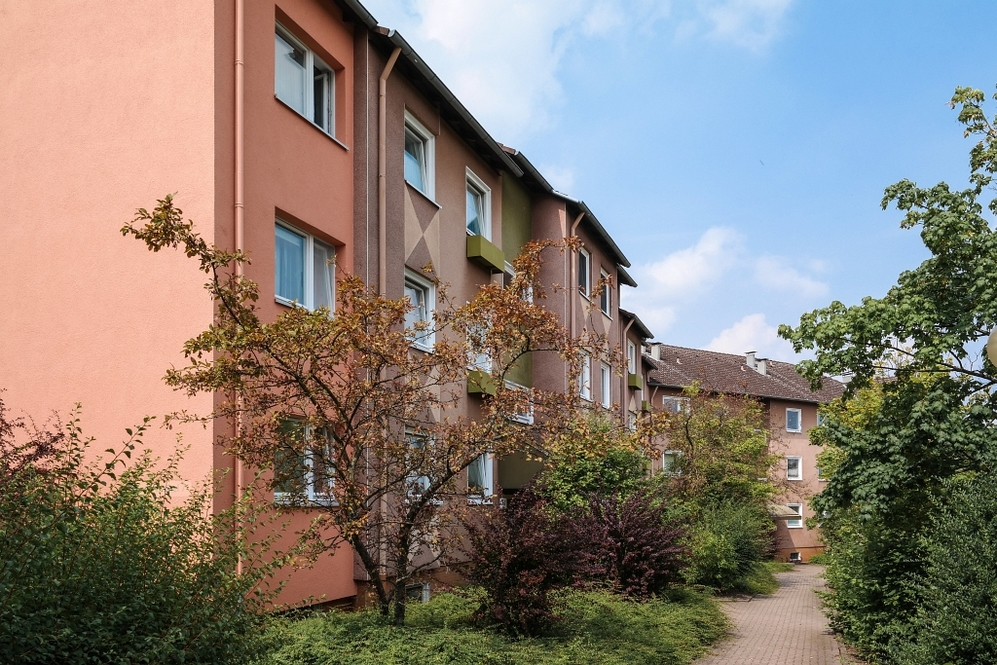Mehrstöckiges Wohngebäude mit bunten Fassaden und begrüntem Vorgarten unter blauem Himmel.