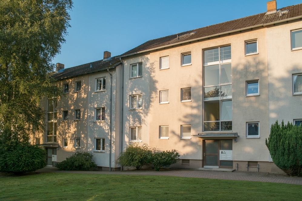 Mehrfamilienhaus mit drei Stockwerken, grüner Vorgarten und klarer Himmel im Abendlicht.
