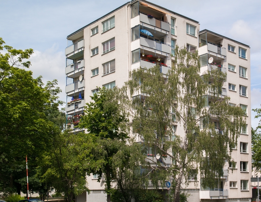 Mehrgeschossiges Wohnhaus mit Balkonen, umgeben von Bäumen und Grünflächen.