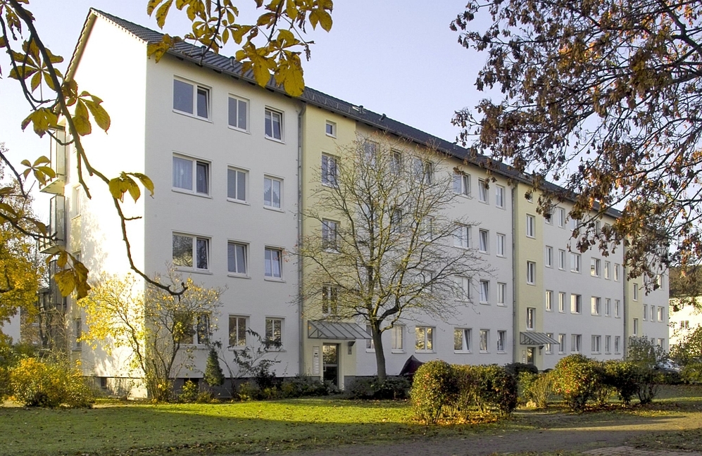 Mehrfamilienhaus mit vier Stockwerken, umgeben von Bäumen und Grünflächen im Herbst.