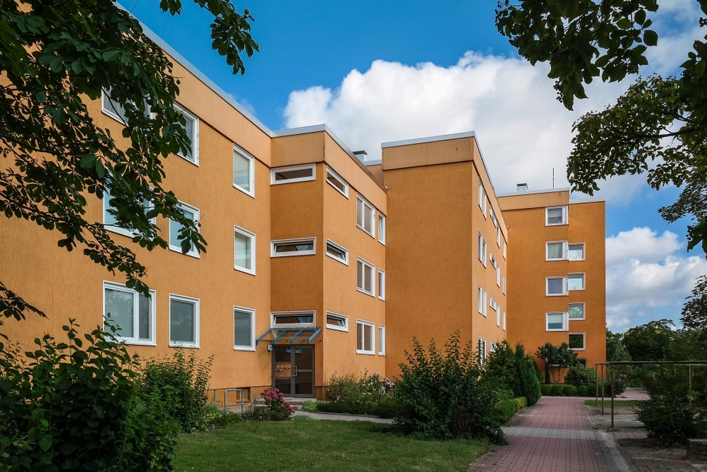 Mehrstöckiges orangefarbenes Wohngebäude mit Grünflächen und Weg unter blauem Himmel.