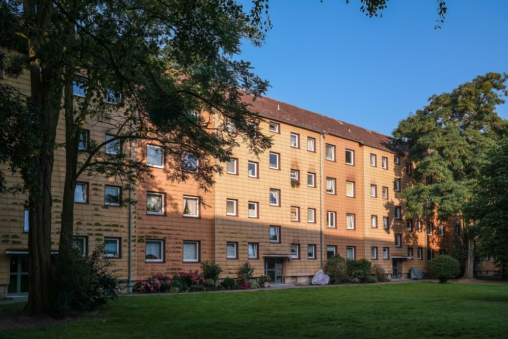 Mehrstöckiges Wohngebäude mit gelber Fassade, umgeben von Bäumen und Rasenfläche.