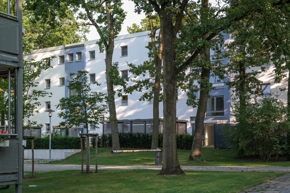 Mehrgeschossige Wohnhäuser mit weißer Fassade, umgeben von Bäumen und Grünflächen.