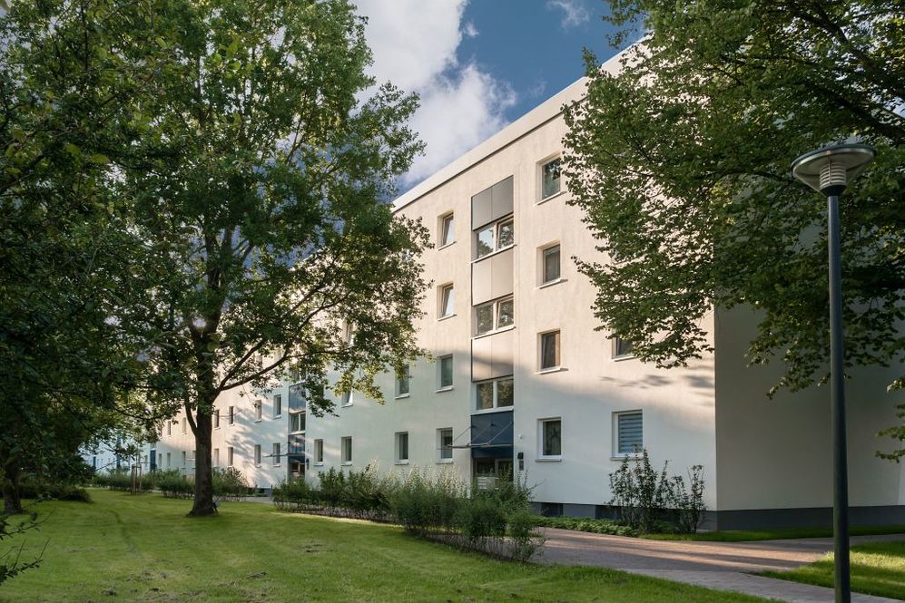 Moderner Wohnblock mit hellen Fassaden, umgeben von Bäumen und gepflegtem Grün.