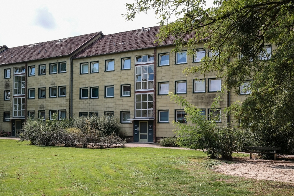 Mehrfamilienhaus mit grüner Außenanlage und Büschen in urbaner Wohnumgebung.
