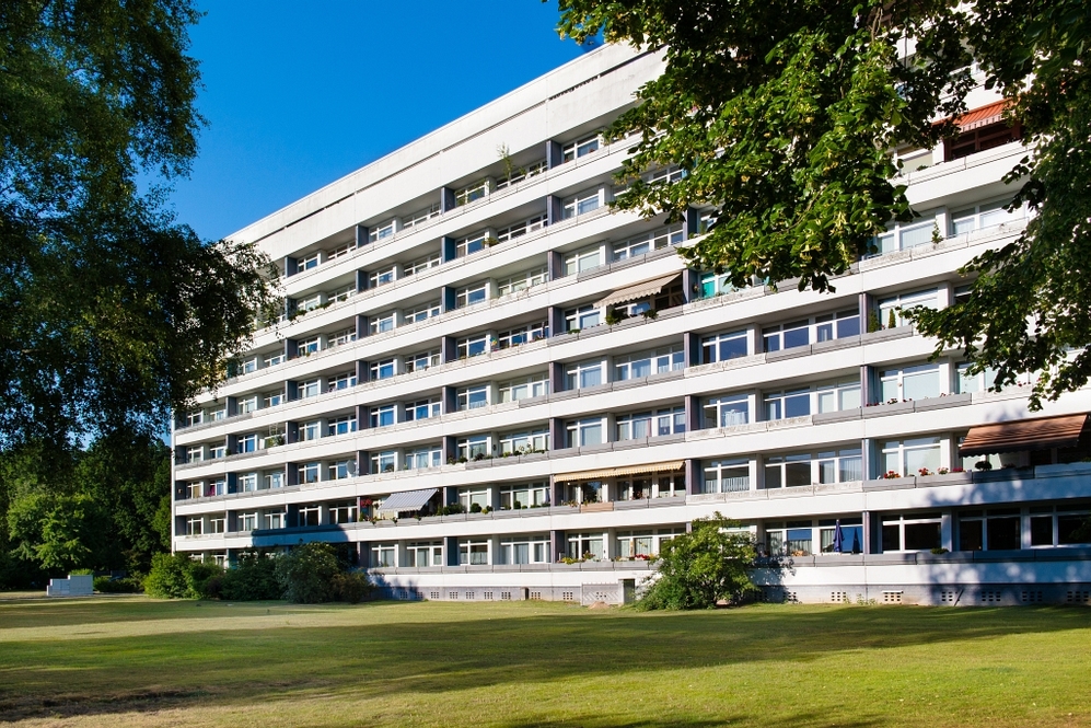 Mehrstöckiges Wohngebäude mit Balkonen, umgeben von Grünflächen und Bäumen.